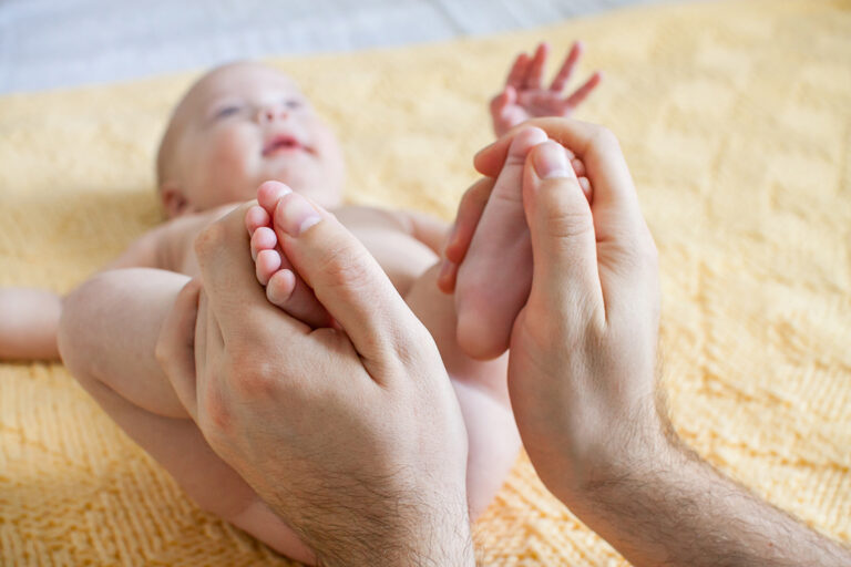 Young father makes massage for happy infant baby on a yellow kni
